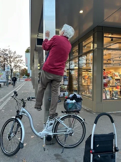 Ein Rentner steht auf einem Velo, um Kleber zu entfernen.